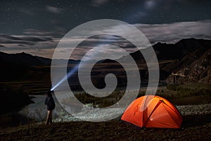 Male tourist with flashlight near his camp tent at night.