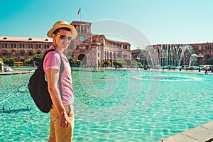 Male tourist in hat with backpack on central square of Yerevan. Caucasian adult man alone explore Armenia. Touristic architecture