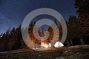 Male tourist have a rest in his camp near the forest at night under beautiful night sky full of stars