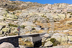 Male tourist hiking on stone bridge, trail to the Laguna Grande de Gredos, Spain photo