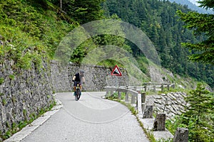 Male tourist pedals an electric bike up a steep road in the Slovenian mountains.