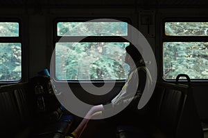 A male tourist rides in a dark train through the woods and looks out the window