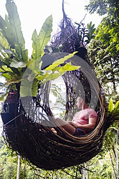 A male tourist is sitting on a large bird nest on a tree at Bali island