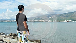 Male tourist standing on rock and enjoying ocean. Concept. Back view of a man standing on a rock cliff and facing the