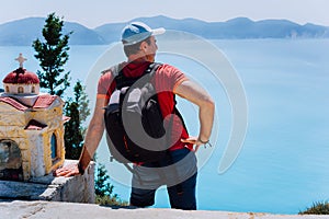 Male tourist staying near small Hellenic shrine Proskinitari admire seascape landscape. Amazing coatline view in the