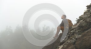 Male tourist on top of mountain in fog in autumn