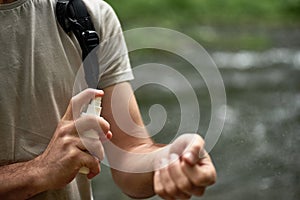 Male tourist using mosquito and tick repellent spray outdoors during hiking