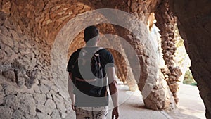 Male tourist is walking alone in alley of artificial grotto with columns in park