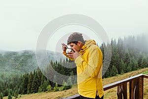 Male tourist in a yellow jacket stands on the terrace of a country house and has breakfast from a plate on a background of