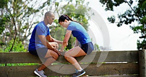 Male trainer assisting fit woman to climb over wooden wall during obstacle course 4k