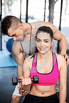 Male trainer assisting woman lifting dumbbell