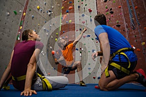 Male trainer guiding athletes in wall climbing at gym