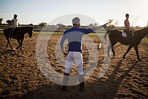 Male trainer guiding young women in riding horse