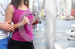 Male trainer help young fitness woman execute exercise with exercise-machine
