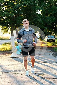 A male trainer is running down the road wearing headphones. Runner in the morning in the park. Listens to music