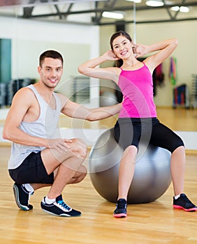 Male trainer with woman doing crunches on the ball