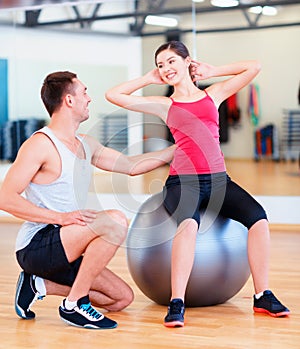 Male trainer with woman doing crunches on the ball
