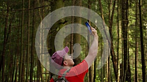 Male traveler with backpack in forest looking for cellular network signal, camera tracking