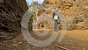 A male traveler with a backpack walks past large brown rocks in the mountains of Poland