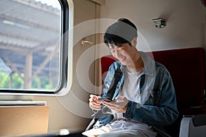 A male traveler backpacker using his smartphone while sitting in his seat on a train