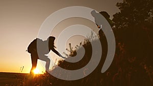 Male traveler holds out his hand to a female traveler climbing hilltop. Tourists climb mountain in sunset, holding hands
