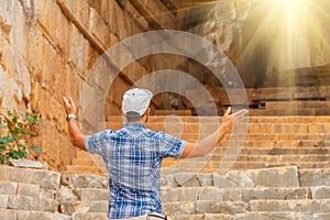 Male traveler in a plaid shirt and shorts explores the ruins of an ancient building at the entrance to the arch with bright light