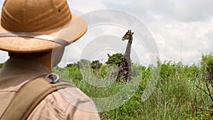 male traveler in safari style photographs a giraffe in the savannah