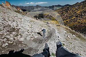 Male Traveler Sits On Top Mountain And Enjoys Mountain View In Summer. Group Of Tourists Climbs Uphill. Point Of View Shot