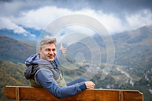 Male Traveler Sitting on Observation Deck Bench Admiring Majestic Mountains Landscape