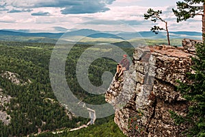 A male traveler is sitting on a rock with a bird`s-eye view of the forest. The concept of recreation and tourism. A man traveler