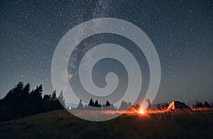 Male traveler standing near campfire and pointing at stars.