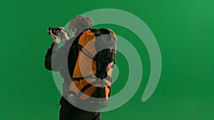 A male traveler takes pictures with a camera while hiking. A tourist with a backpack on his back stands in a studio on a