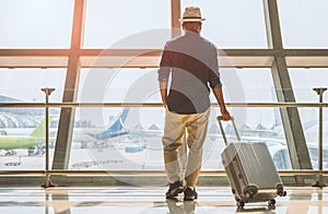 A male traveler wearing a gray hat Preparing to travel He has a trolley bag He stands at a large airport for traveling around the