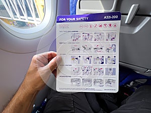 Male traveler on WizzAir airplane flight reading safety brochure before taking off