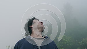 Male traveller flicks hair at the top of mountain with thick fog in the early morning in the background. Lifestyle on vacation.