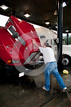 Male truck driver closing hood of 18-wheeler