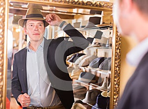 Male try on trilby hat and looking at mirror in headwear boutique