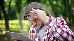 Male trying to read newspaper in park, poor sight, farsightedness, myopia