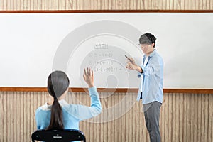 Male tutor standing in front of whiteboard is smiling and pointing to him for ask question and asian young boy