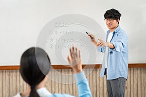 Male tutor standing in front of whiteboard is smiling and pointing to him for ask question and asian young boy