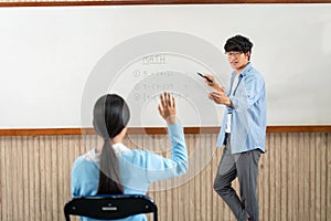 Male tutor standing in front of whiteboard is smiling and pointing to him for ask question and asian young boy