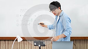 Male tutor standing in front of whiteboard and writing math equations on board to explaining new lesson