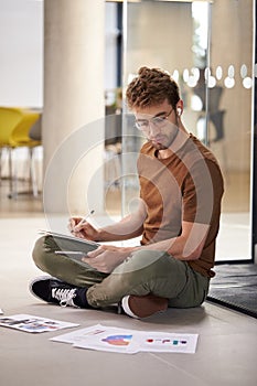 Male University Student On Floor Of College Building With Digital Tablet Wearing Earbuds