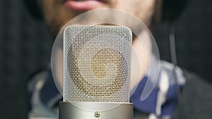 Male unrecognizable singer singing song into the microphone at sound studio. Young man recording new melody or song