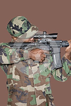 Male US Marine Corps soldier aiming M4 assault rifle over brown background