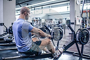 Male using rowing machine at fitness club. Young man doing exercises on fitness machine in gym. Side view