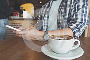 Male using a smart phone with coffee cup on wooden table