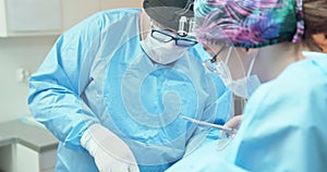 Male veterinarian, in glasses, white gloves, cap and in surgical outfit, while he sutures the operated dog's leg