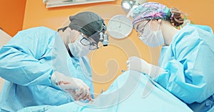Male veterinarian, in glasses, white gloves, cap and in surgical outfit, while he sutures the operated dog's leg