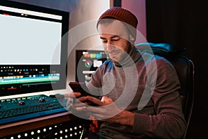 Male Video Editor sitting at his Computer using phone photo